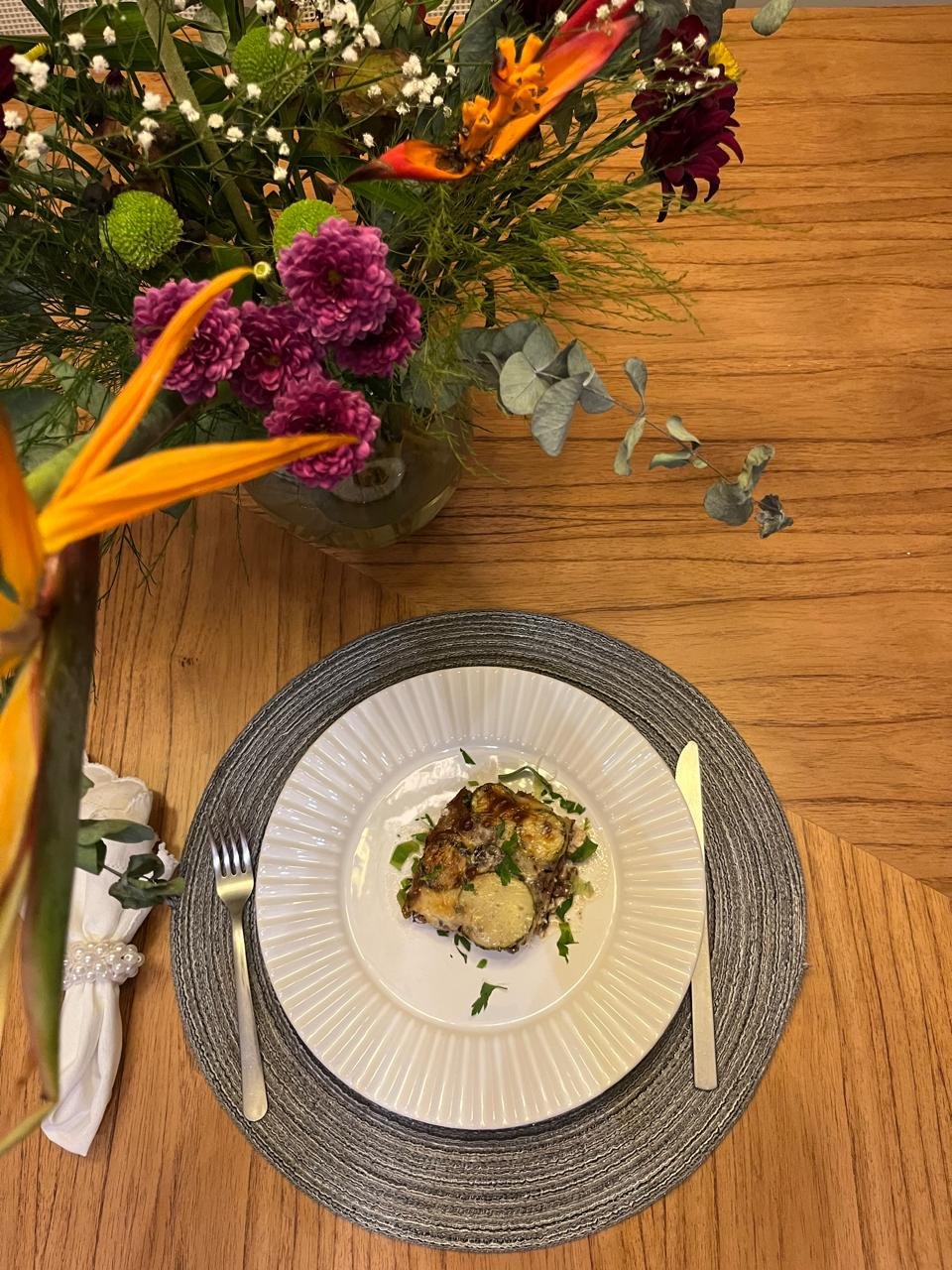 Abobrinha gratinada servida em mesa posta com arranjo floral