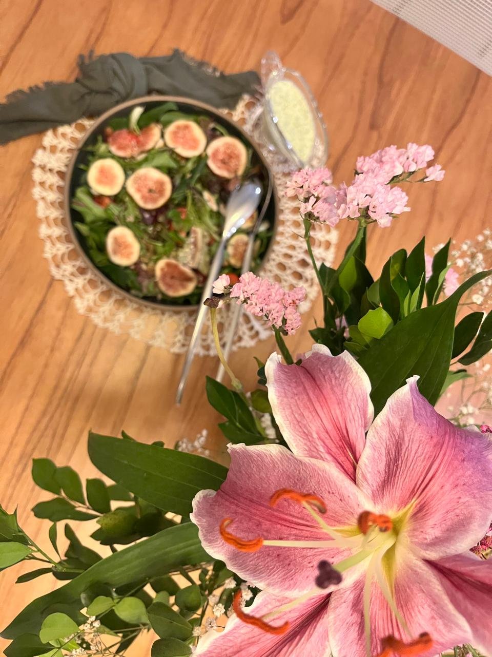 Mesa com flores em primeiro plano, salada ao fundo e molho de iogurte servido